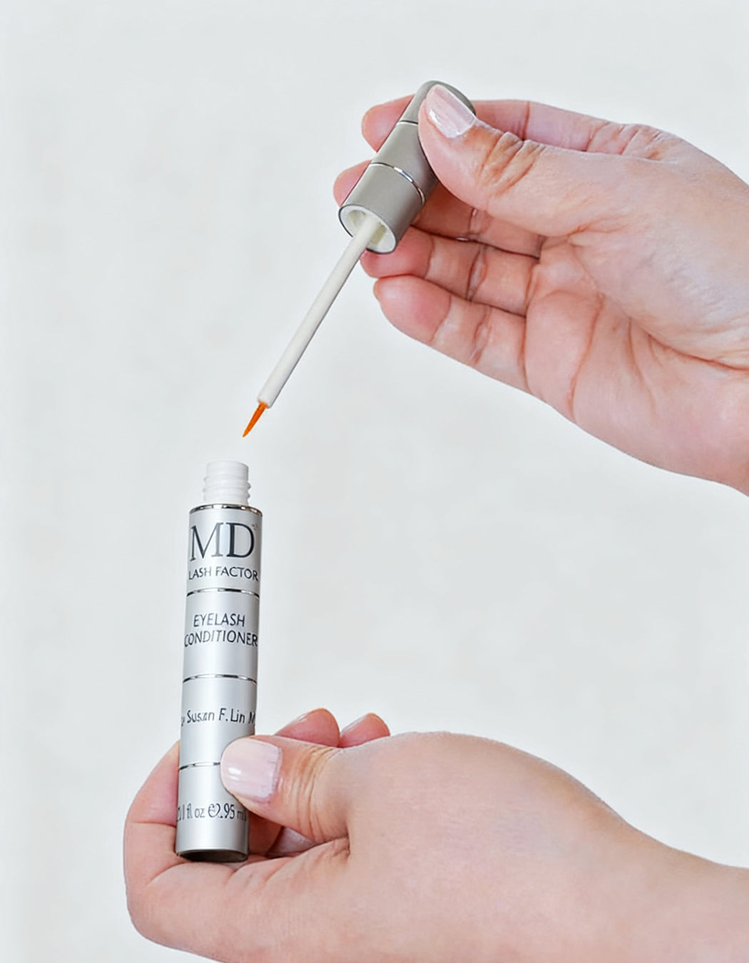 Elegant photo of two hands holding MD Lash Factor Eyelash Conditioner tube and precision brush tip – premium lash growth conditioner for longer, fuller lashes by MD Lash"